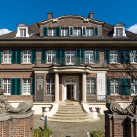 A view of the exterior of Villa ten Hompel. The front door is invitingly open.