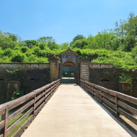 Eine Brücke läuft auf das Tor der Festung zu. Oberhalb ist ein Schild angebracht, auf dem der Schriftzug Fort Queuleu steht.