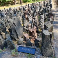Tat- und Gedenkort Bikernieki (Foto: Villa ten Hompel) Auf einer Wiese steht ein Denkmal, bestehend aus zahlreichen, aufgerichteten, unterschiedlich großen Steinen in einem Viereck.