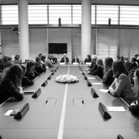 Ein Schwarzweißbild der Podiumsdiskussion: Die Teilnehmenden sitzen an einem Konferenztisch und hören den Redner*innen Eva Szepesi, Marcel Reif und der Bundestagspräsidentin Bärbel Bas vor Kopf zu.