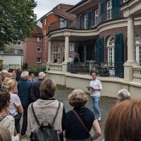Ein Mann steht hinter der Villa ten Hompel vor einer Menge Menschen