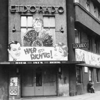 Auf einem Schwarz-Weiß-Foto ist eine Straße und ein mehrstöckiges Haus zu sehen. Auf der Fassade ist der Name 'Eldorado' angebracht und eine Werbeanzeige mit dem Schriftzug 'Hier ist's richtig!'.
