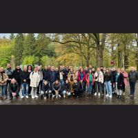 Gruppenfoto mit Menschen unter Bäumen auf einem geteerten Weg.