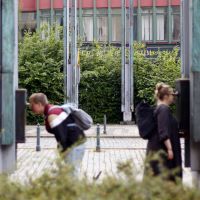 Zwei Teilnehmende schauen durch Guckröhren an grünen Stelen an der Stelle der ehemaligen Brücke.