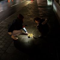 zwei Menschen beleuchten mit Kerzen und Taschenlampen drei Stolpersteine