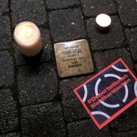 zwei Kerzen und Flyer der Aktion "Deportationen sichtbar machen" neben dem Stolperstein von Carl Hein