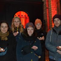 fünf junge Menschen vor dem rot beleuchteten Gebäude am Kanonengraben 4 in Münster halten Teelichter in der Hand