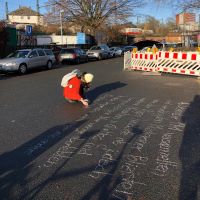 Kim Sommerer schreibt mit Kreide einen Infotext auf die Straße vor dem ehemaligen Güterbahnhof