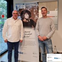 Thomas Köhler und Peter Römer stehen vor einem Aufsteller der Stiftung EVZ zur Bildungsagenda NS-Unrecht