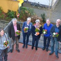 Mitglieder des Vorstands stehen nebeneinander auf dem Balkon der Villa und halten Blumensträuße in der Hand