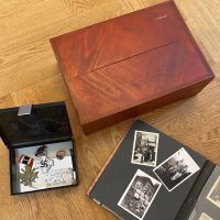 rot lackierte geschlossene Kiste, daneben ein geöffnetes Fotoalbum mit Schwarz-weiß-Fotos und eine geöffnete Schatulle mit Abzeichen