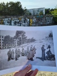 Ein historisches Foto von Polizisten in Prora wird in die Kamera gehalten, im Hintergrund ein mittlerweile renovierter Gebäudekomplex