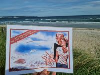 historisches Propagandaplakat mit einem Pärchen und Meeresblick wird in die Kamera gehalten, im Hintergrund Strand und Meer