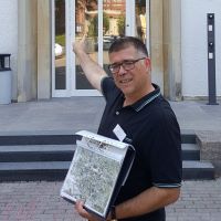 Mann mit Stadtplan in der Hand weist auf das Gebäude hinter ihm