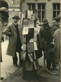 Ab dem 6. Mai 1933 wurden die Werke von den Nationalsozialisten als „undeutsch“ verunglimpfter Autor*innen vor dem Fürstenberghaus gesammelt und an einem „Schandpfahl“ angeheftet. Am 10. Mai 1933 wurden die zusammengetragenen Bücher dann auf dem heutigen Schlossplatz verbrannt. Quelle: Stadtarchiv Münster Historisches Foto eines Schandpfahls mit angehefteten Buchdeckeln und einiger Personen, die sich den Pfahl anschauen