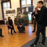 links zwei sitzende Teilnehmende der Führung, die zwei Mitarbeitern der Villa ten Hompel rechts zuhören