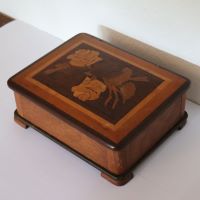 Auf einem Tisch steht ein Holzkästchen, ungefähr die Größe eines Nähkästchens, mit Einlegearbeiten aus unterschiedlichem Holz, die mehrere Rosen bilden.