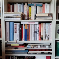 In einem weißen Bücherregal stehen zahlreiche Bücher zum Holocaust und der NS-Zeit, teils vor- und übereinander. Rechts und links erkennt man noch weitere Bücherregale.