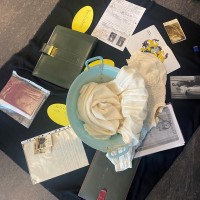 Auf einem Tuch liegen verschiedene historische Objekte wie Fotos oder Bücher, aber auch ein Waschzuber und ein weißes Kleid.