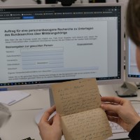 Eine Person sitzt vor einem Computerbildschirm und blickt auf einen Feldpostbrief.