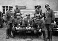 Das Schwarzweißfoto ist eine Gruppenaufnahme: Sieben Polizisten in Uniform sitzen und setzen um ihre Fahrzeuge herum, im Hintergrund steht ein verputztes Gebäude.