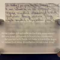 Zu sehen ist ein Faksimile des Briefs von Nina aus dem Ghetto Lublin und eine Plakette, die die Handschrift übersetzt. Zu lesen ist 'Meine Lieben (ich schreibe an Euch alle zusammen)! Bei uns braut sich etwas Schreckliches zusammen... Bei uns herrscht Panik. Ich habe schreckliche Angst. Ich küsse Euch Nina. Einzelheiten im nächsten Brief.'