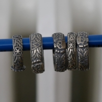 Auf einem blauen Buntstift hängen fünf Ringe aus Silber. Sie sind ähnlich dekoriert, nämlich mit je einem Totenkopf, Runen und Blättern.
