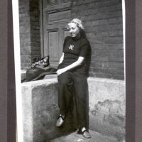 Auf einem Schwarzweißfoto lehnt Henriette Hertz an einer Häuserwand, sie selbst blickt lächelnd aus dem Bild heraus. Sie trägt schicke Kleidung und modische Schuhe.