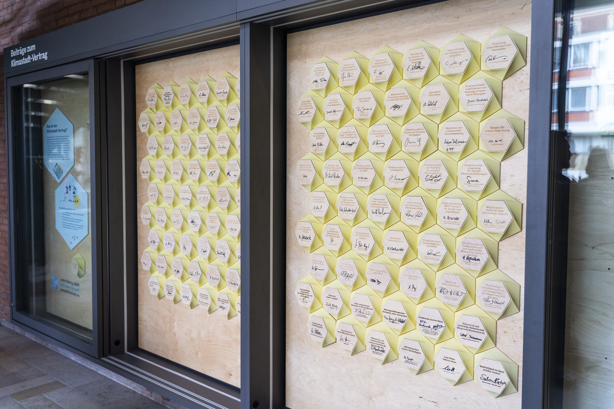 Eine Vitrine mit vielen sechseckigen gelben Plaketten, die an einer Wand befestigt sind, einige Zettel mit handschriftlichen Notizen