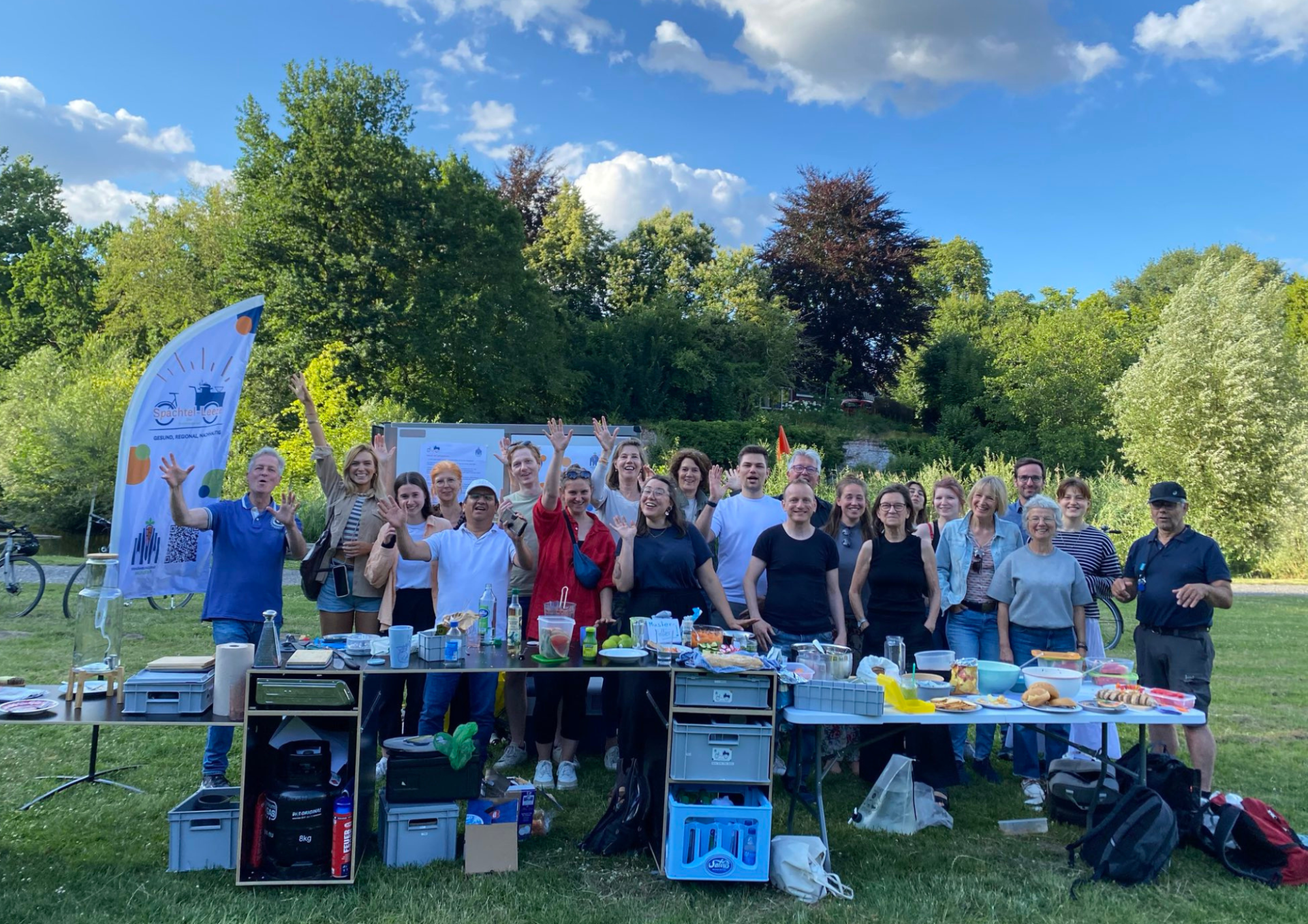 Ein Foto einer Gruppe Menschen hinter einem aufgebauten Buffet auf einer Wiese