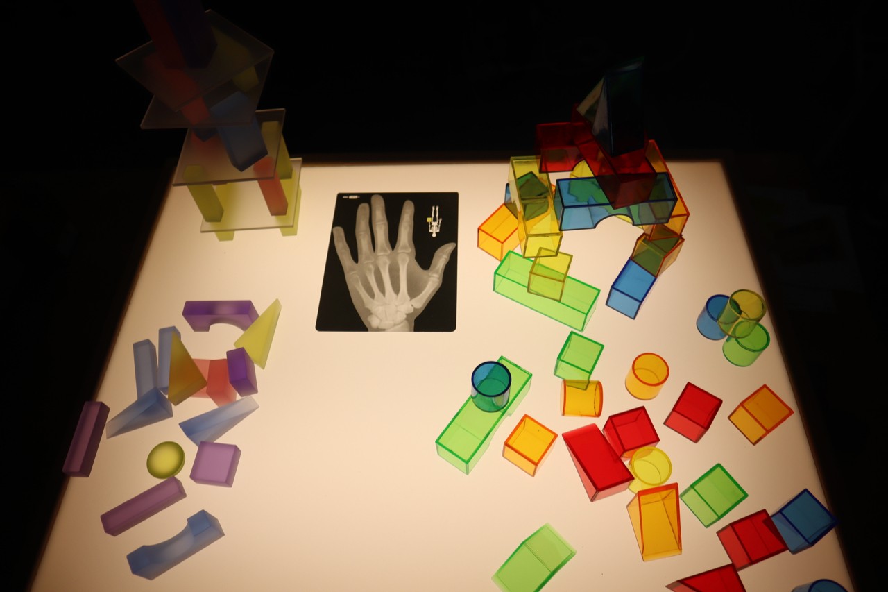 Leuchtender Tisch mit farbigen, transparenten geometrischen Formen und einer Röntgenaufnahme einer Hand in der Mitte