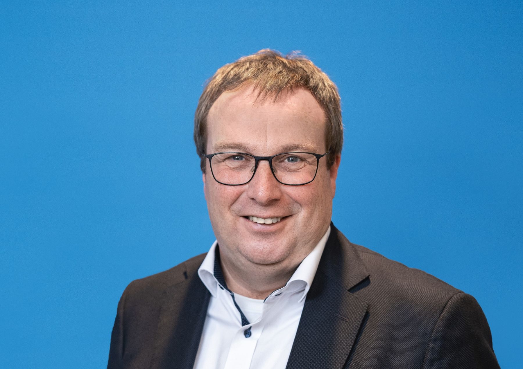 Mann mittleren Alters mit Brille, schwarzem Sako und weißem Hemd