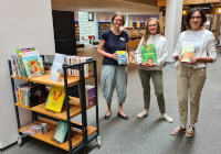 Übergabe der ukrainischen Buchspende Drei Frauen vor einem Rollregal halten Bücher in den Händen