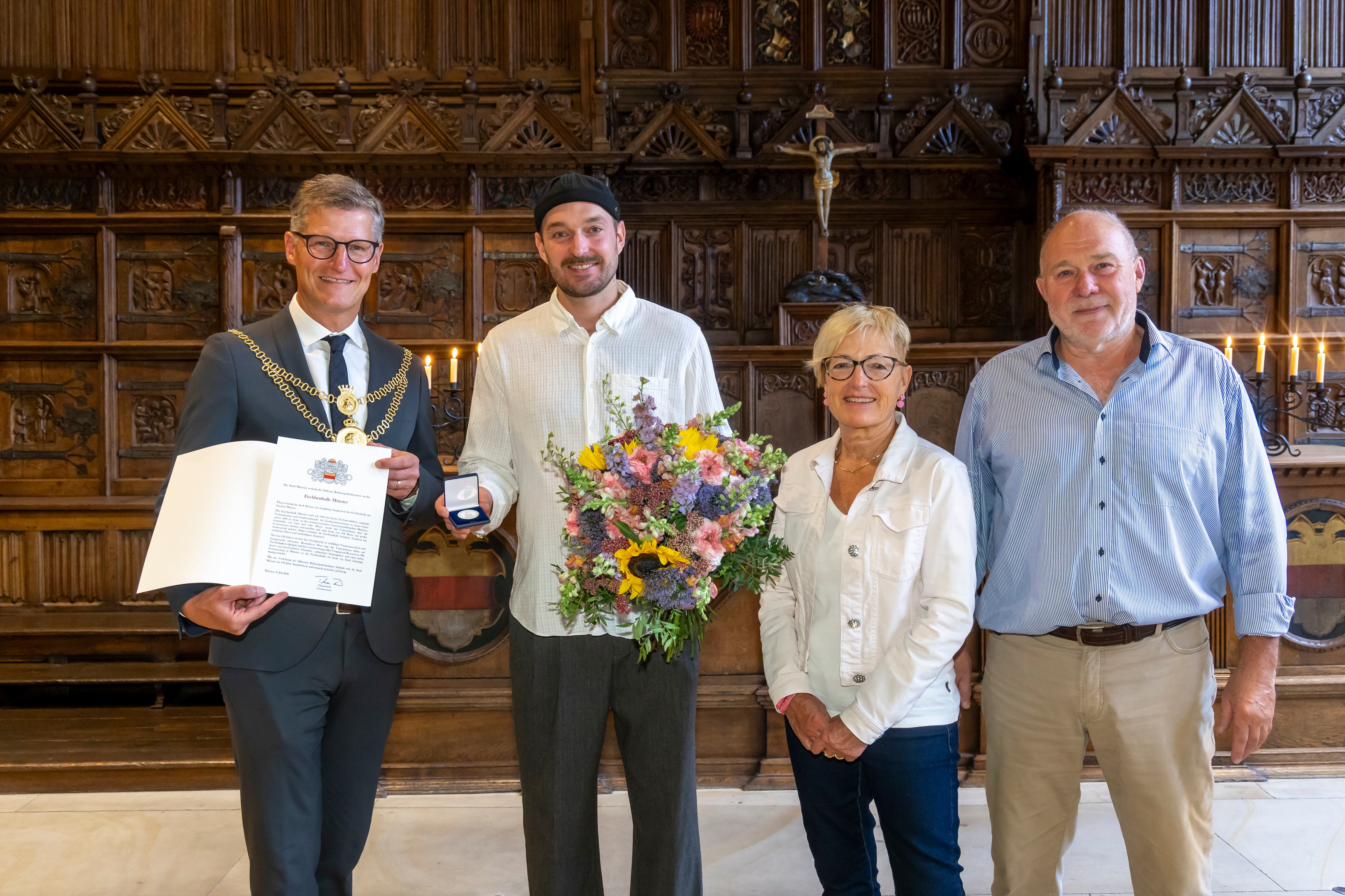 Gruppenbild mit vier Personen, Urkunde, Münze und Blumenstrauß