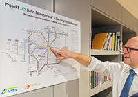 Markus Lewe vor dem Ausbauplan „S-Bahn Münsterland“ Markus Lewe zeigt auf einen großen S-Bahn-Plan.