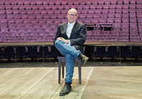 Markus Lewe im Theater Münster Markus Lewe sitzt auf einem Stuhl vor den Sitzreihen im Großen Haus des Theaters.
