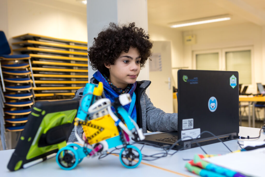 Ein Junge sitzt an einem Computer an den ein Roboter angeschlossen ist