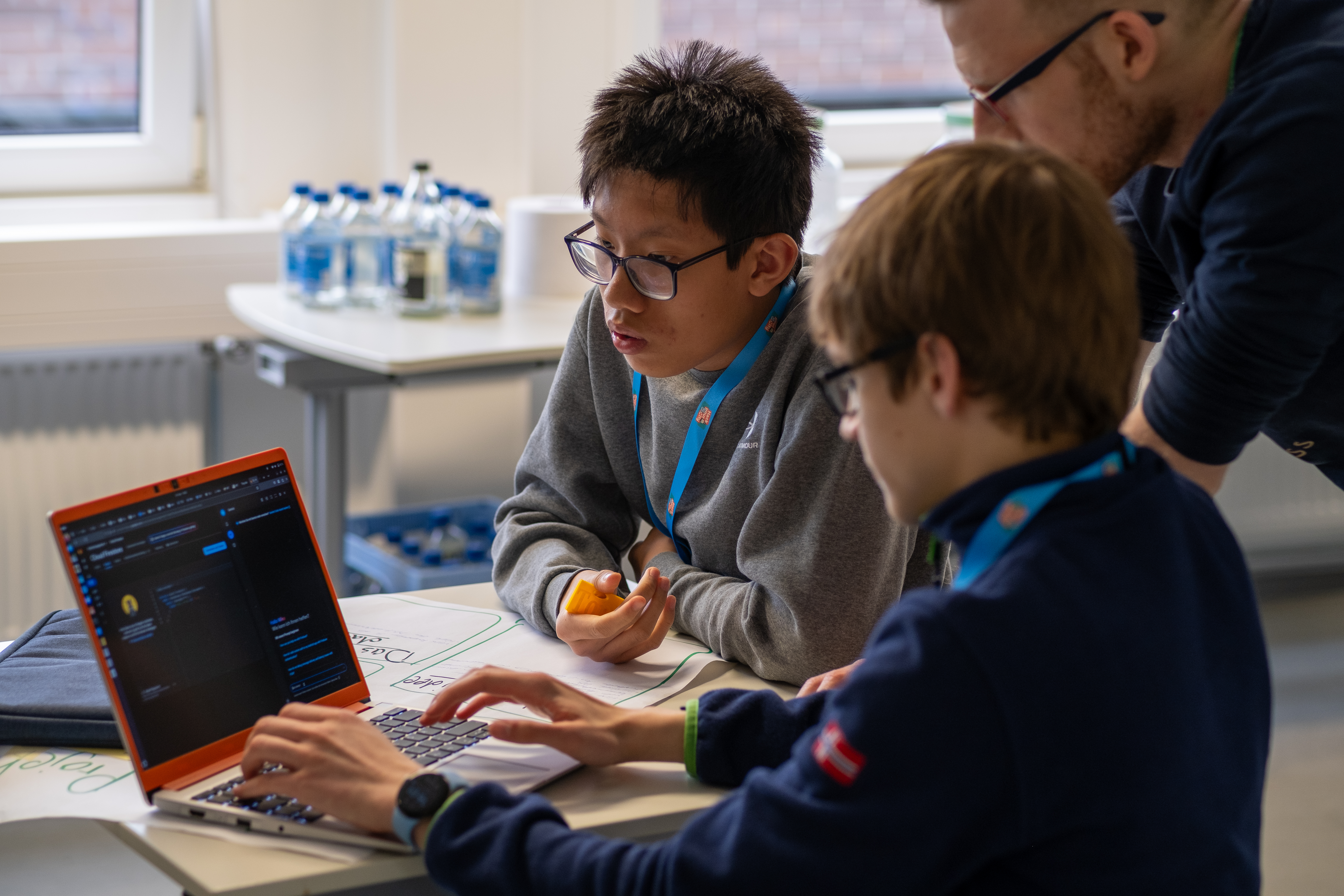 2 Jungs sitzen an einem Computer und bekommen etwas erklärt von einem Mentor