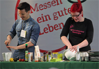 Foto: Daniel Sechert Zwei kochende Personen auf einer Bühne an einem Tisch voller Zutaten