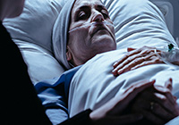 Schwerkranker Mensch im Klinikbett. Schwerkranker Mensch im Klinikbett liegt mit geschlossenen Augen da. Jemand hält seine Hand.