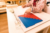Montessori-Tafel für Rechenaufgaben Schreibtisch, an dem eine Person vor einer blau-roten Montessori-Mathematiktafel sitzt.